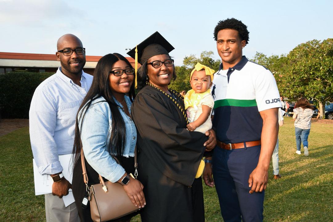 Graduate poses with family outside of Reed Green Coloseum after commencement. 